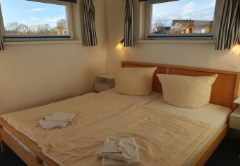 Acogedor dormitorio en una casa flotante en Alemania con cama doble y luz natural desde las ventanas.