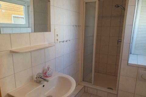 Bright bathroom on a houseboat featuring a shower, sink, mirror, shelf, and window with a view.