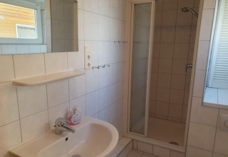 Bagno luminoso su una casa galleggiante con doccia, lavandino, specchio, mensola e finestra.
