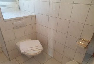 Small bathroom on a houseboat in Germany with a wall-mounted toilet, towels, and a toilet paper holder.