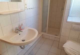 Bright bathroom with sink, mirror, shower stall, and toilet inside a houseboat in Germany.