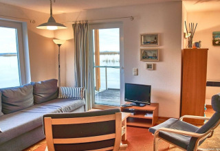 Gezellige woonkamer op een woonboot met bank, stoelen, tv en ramen met uitzicht op het water.