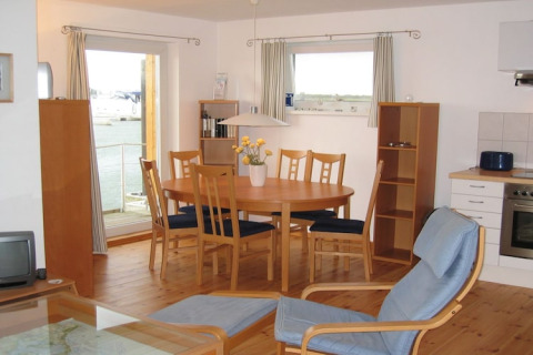 Heldere eethoek en keuken op een woonboot met houten stoelen en uitzicht op het water buiten.