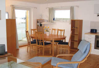 Bright dining and kitchen area on a houseboat with wooden chairs and a view of the water outside.