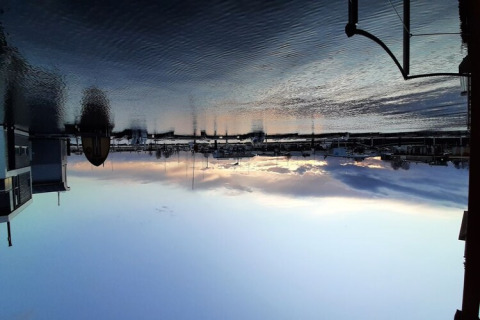 Zonsondergang vanuit een woonboot, kalm water en boten in de haven, lucht mooi gereflecteerd.