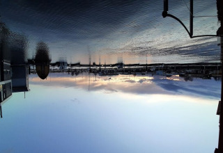 Zonsondergang vanuit een woonboot, kalm water en boten in de haven, lucht mooi gereflecteerd.