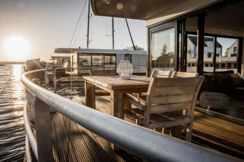 Zonsondergang uitzicht vanaf houseboat 475077 in Duitsland met houten terras, tafel, stoelen en water.