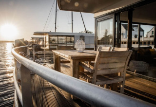 Zonsondergang uitzicht vanaf houseboat 475077 in Duitsland met houten terras, tafel, stoelen en water.