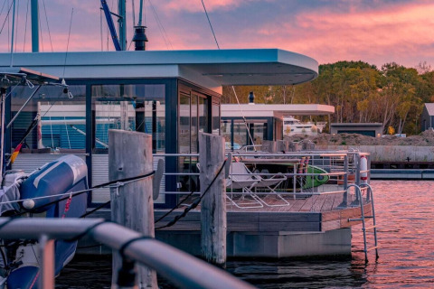 Woonboot genaamd 475077 aangemeerd in Duitsland bij zonsondergang, met ligstoelen op het dek.
