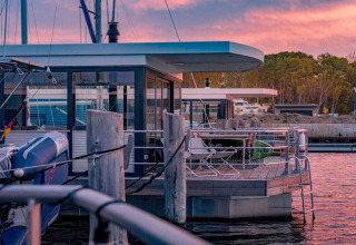 Woonboot genaamd 475077 aangemeerd in Duitsland bij zonsondergang, met ligstoelen op het dek.