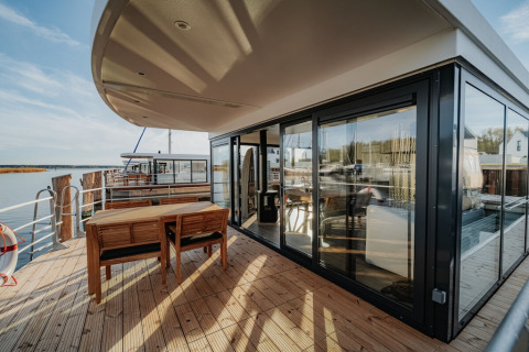 Buitenterras van woonboot «475077» in Duitsland met eettafel, stoelen en uitzicht over het water.