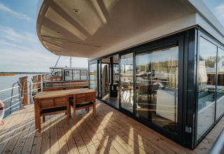 Buitenterras van woonboot «475077» in Duitsland met eettafel, stoelen en uitzicht over het water.