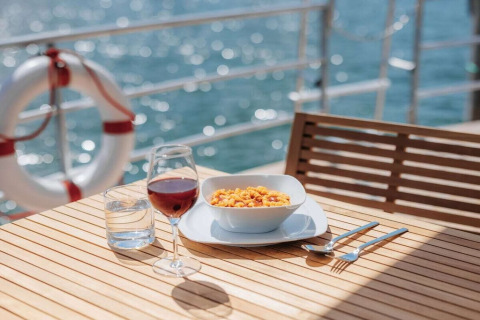 Maaltijd met pasta, wijn en water op houten tafel op woonboot '475077' met uitzicht op water in Duitsland.