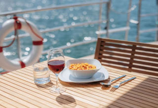 Maaltijd met pasta, wijn en water op houten tafel op woonboot '475077' met uitzicht op water in Duitsland.