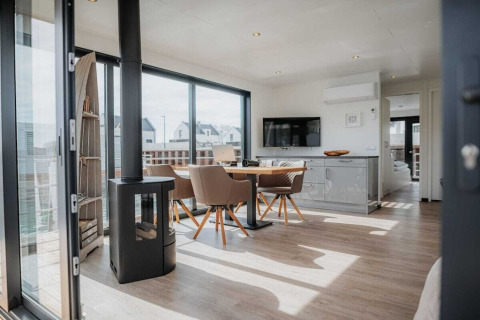 Modern woonbootinterieur met eettafel, kachel, grote ramen en uitzicht op het water in Duitsland.