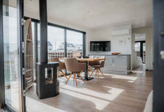 Modern woonbootinterieur met eettafel, kachel, grote ramen en uitzicht op het water in Duitsland.