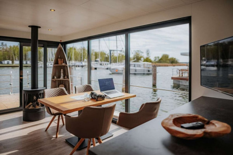 Modern interieur van een woonboot met grote ramen, haard en uitzicht op jachthaven in Duitsland.