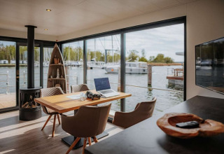Modern interieur van een woonboot met grote ramen, haard en uitzicht op jachthaven in Duitsland.
