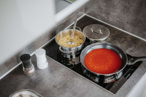 Keuken op een woonboot met een pan pasta en een koekenpan tomatensaus op het fornuis in Duitsland.