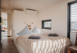 Knusse slaapkamer met tweepersoonsbed op woonboot «475077» in Duitsland, veel zonlicht door ramen.
