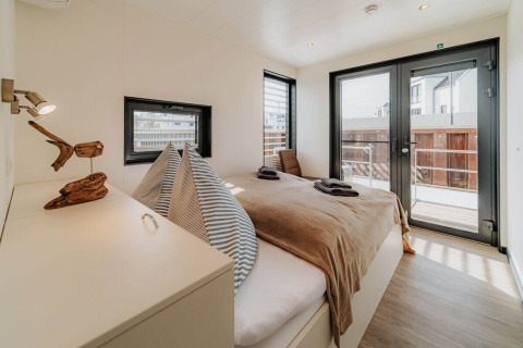 Lichte, moderne slaapkamer met tweepersoonsbed en grote ramen op woonboot «475077» in Duitsland.