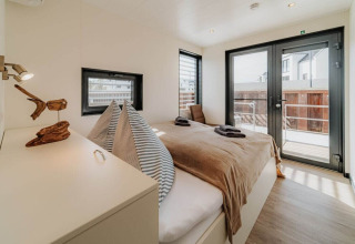 Lichte, moderne slaapkamer met tweepersoonsbed en grote ramen op woonboot «475077» in Duitsland.