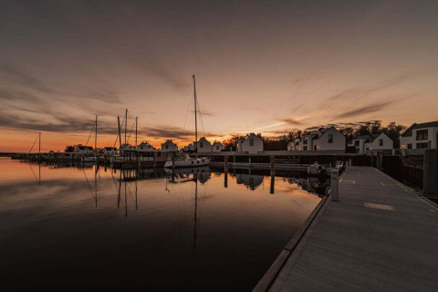 Zonsondergang bij een rustige jachthaven in Duitsland met woonboten en witte huizen weerspiegeld in het water.