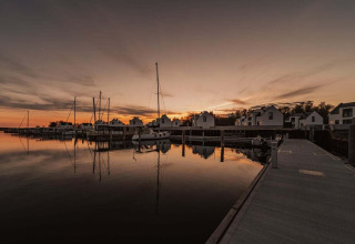 Zonsondergang bij een rustige jachthaven in Duitsland met woonboten en witte huizen weerspiegeld in het water.