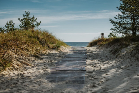 Zandpad tussen duinen en bomen, richting zee vanaf een woonboot aan het strand in Duitsland.
