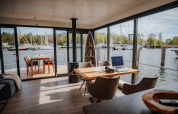 Moderne interiør på husbåd i Peenemünde med udsigt til havn, terrassebord og bærbar computer.
