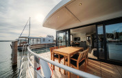 Moderne woonboot in Peenemünde met houten terras, tuinset en uitzicht op het rustige water.
