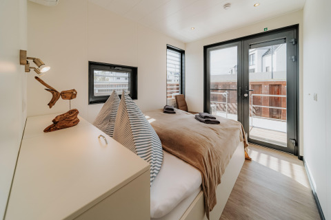 Chambre moderne avec lit double et grandes fenêtres sur une péniche à Peenemünde, avec accès au balcon.