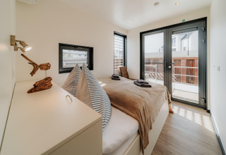 Dormitorio moderno con cama doble y grandes ventanales en una casa flotante en Peenemünde con acceso a balcón.