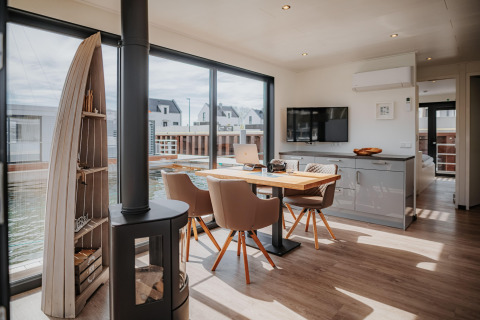 Lyst og moderne interiør på en husbåd i Peenemünde med spisebord, pejs og store vinduer mod vandet.