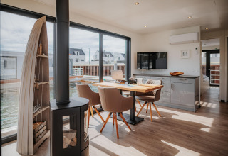 Interior moderno y luminoso de una casa flotante en Peenemünde, con mesa de comedor, chimenea y vistas al agua.