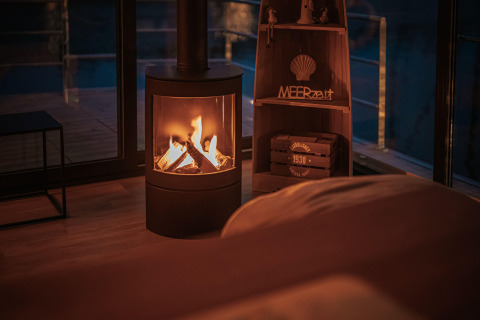 Cozy living space on a houseboat in Peenemünde with a lit fireplace and evening view of the deck.