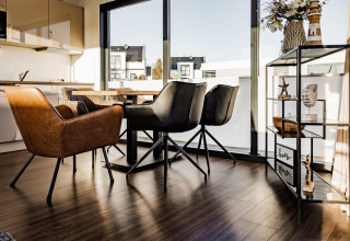 Moderne eethoek op een woonboot in Peenemünde met grote ramen, trendy stoelen en decoratief rek.