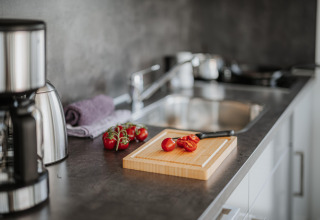 Plan de travail moderne sur une péniche à Peenemünde avec tomates, planche à découper, couteau et cafetière.