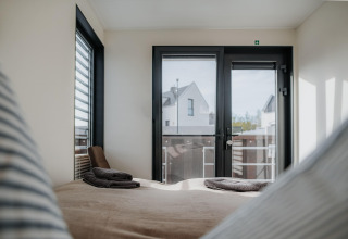 Zicht vanuit een slaapkamer op Houseboat in Peenemünde met opgemaakt bed en grote ramen naar huizen.