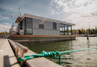 Casa galleggiante moderna a Peenemünde ormeggiata al molo, circondata dall'acqua e un piccolo porto turistico.