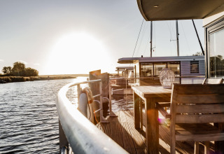 Sunset view from the deck of Houseboat in Peenemünde with waterside seating and wooden furniture.