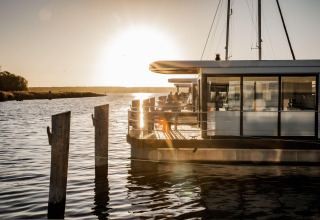 Tramonto dietro una moderna houseboat ormeggiata a Peenemünde, riflessa sull'acqua calma e paesaggio sereno.