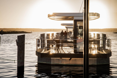 Tramonto su una moderna houseboat a Peenemünde, due persone in piedi sul ponte vicino all'acqua.