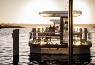 Zonsondergang bij een moderne woonboot in Peenemünde, met twee mensen op het dek aan het water.