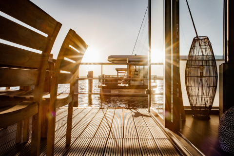 Zonsondergang vanuit Houseboat in Peenemünde met houten terras, designstoelen en rustig water.