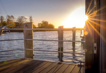 Sonnenuntergang über dem Wasser von einem Hausboot in Peenemünde mit Geländer und Sonnenstrahlen.