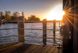 Atardecer visto desde una casa flotante en Peenemünde, con agua, muelle y rayos de sol entre las barandas.