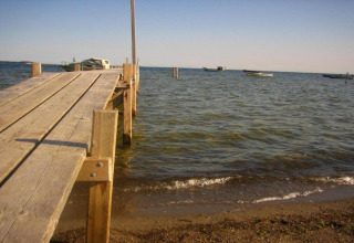 Houten steiger aan het strand met zicht op een woonboot en kleine bootjes in Peenemünde bij zonnig weer.