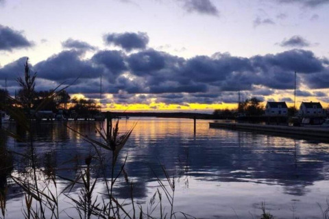 Vista del atardecer desde una casa flotante en Peenemünde, con nubes sobre el agua y casas cerca.