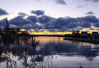 Vista del atardecer desde una casa flotante en Peenemünde, con nubes sobre el agua y casas cerca.
